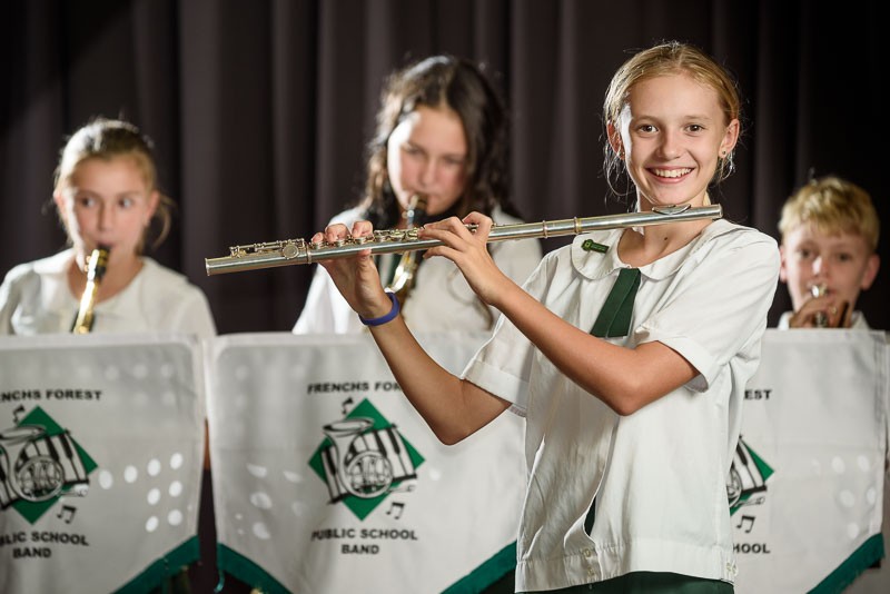 Student playing the flute as a part of the band with other band members playing instruments in the background